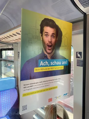 Werbeposter mit überraschter Männermimik im Zug – Kampagnenmotiv für den Nahverkehr Rheinland, fotografiert von nonverbal | businessfotografie.